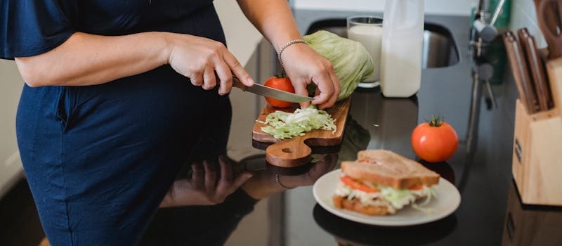 mulher corta alface e tomate em tábua de madeira para fazer uma sanduíche para comer antes do treino