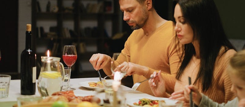 casal e uma filha comem sentados à mesa, com caras sérias